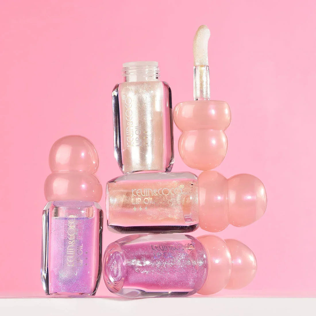 Aceites labiales brillantes KEUM&COCO con glitter, frascos rosa sobre fondo rosa, cosméticos Bibi Boom