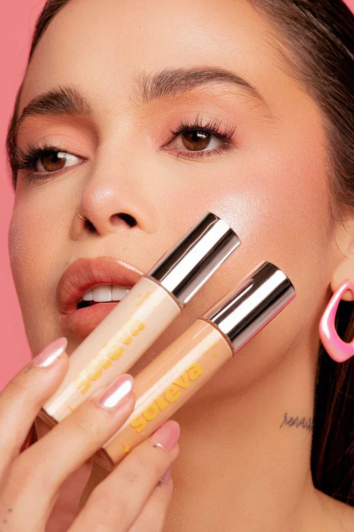 Modelo con maquillaje natural sosteniendo dos correctores Soleva, resaltando su textura cremosa y cobertura alta para el rostro.