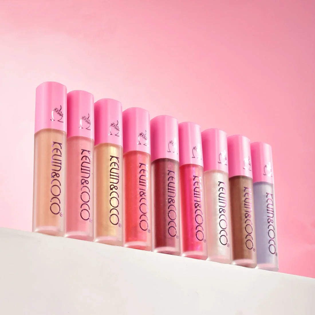 Kit de gloss labial KEUM&COCO en tonos variados, maquillaje Bibi Boom, fondo rosa.