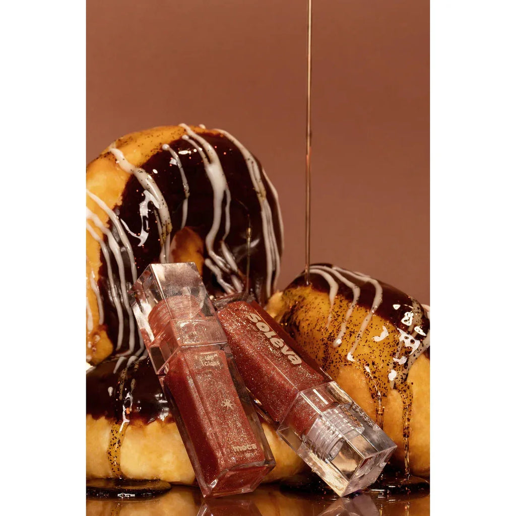 Brillos Labiales Líquidos Soléva tono mocha junto a donas con chocolate, presentación creativa de maquillaje hidratante y luminoso.