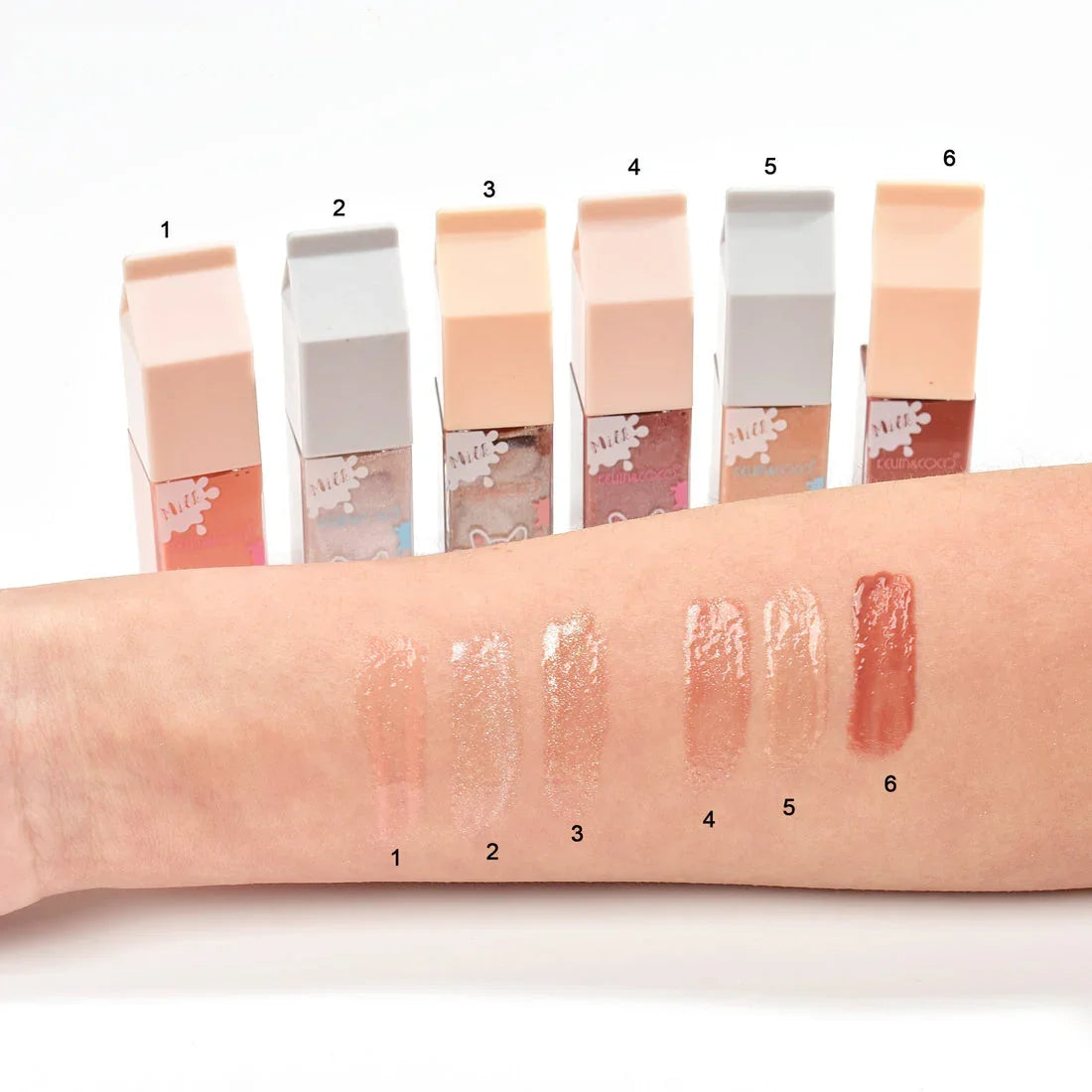 Muestras de gloss labial Bibi Boom en brazo, seis tonos nude y rosados con empaques alineados.