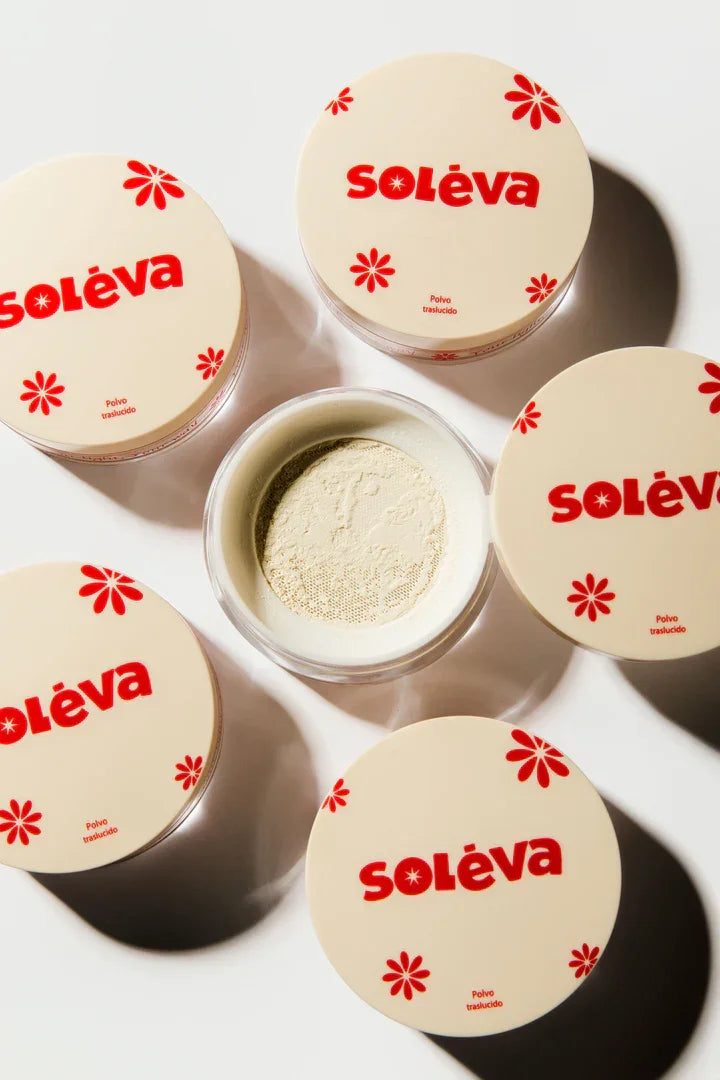 Polvo traslúcido Soléva abierto y rodeado de envases cerrados, diseñado para sellar maquillaje y reducir el brillo con textura ligera.