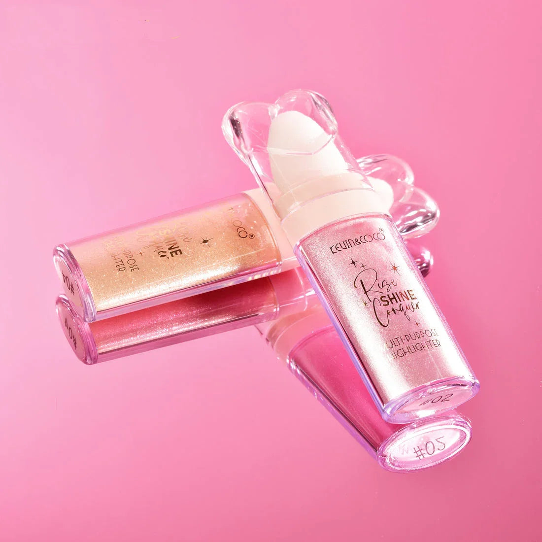 Iluminador en polvo rosa y dorado con envase transparente sobre fondo rosa, maquillaje Bibi Boom